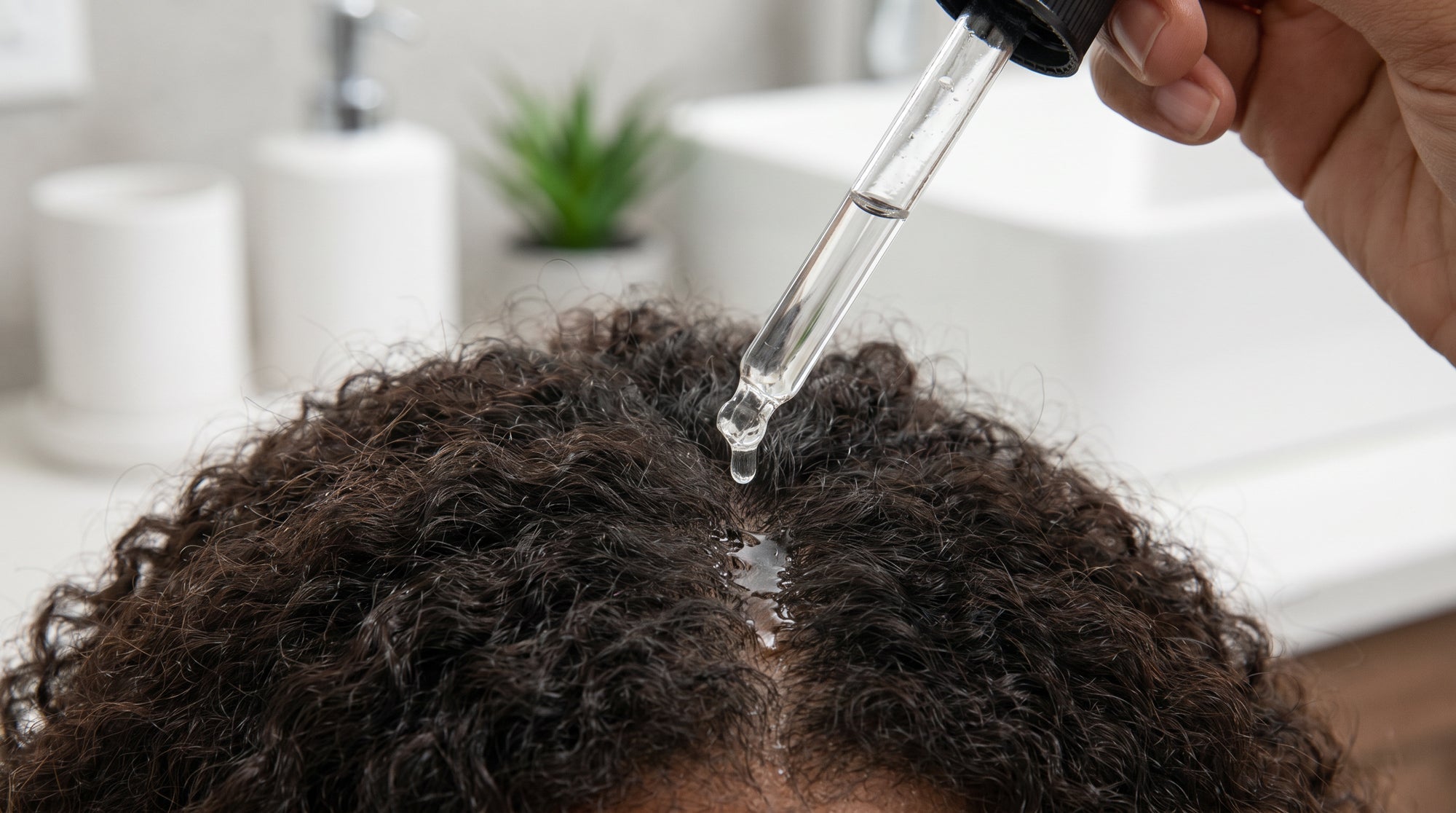A woman with coily hair applying hair growth serum due ton thinning hair